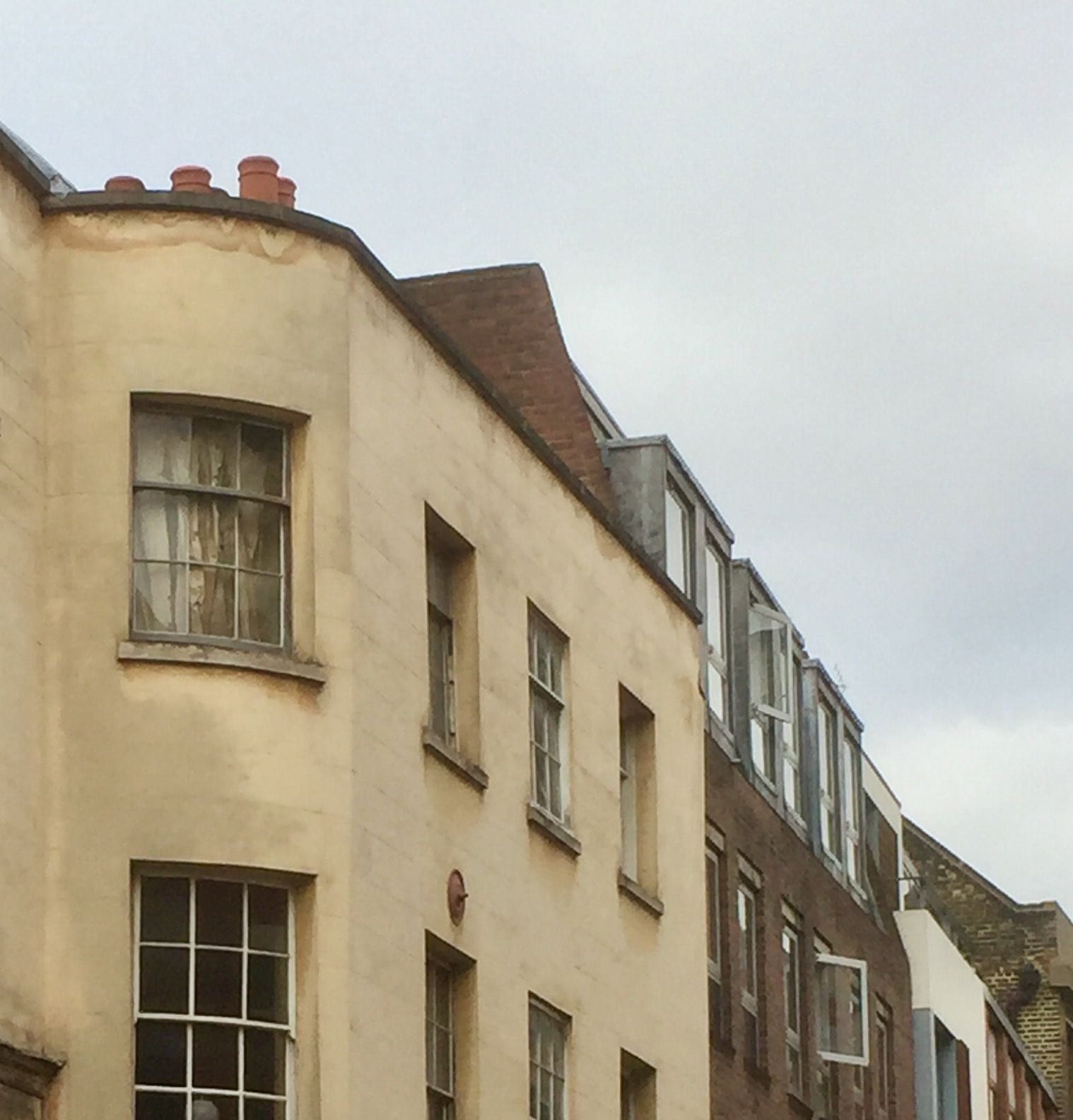 The curved, cream-rendered front of an old house with sash windows